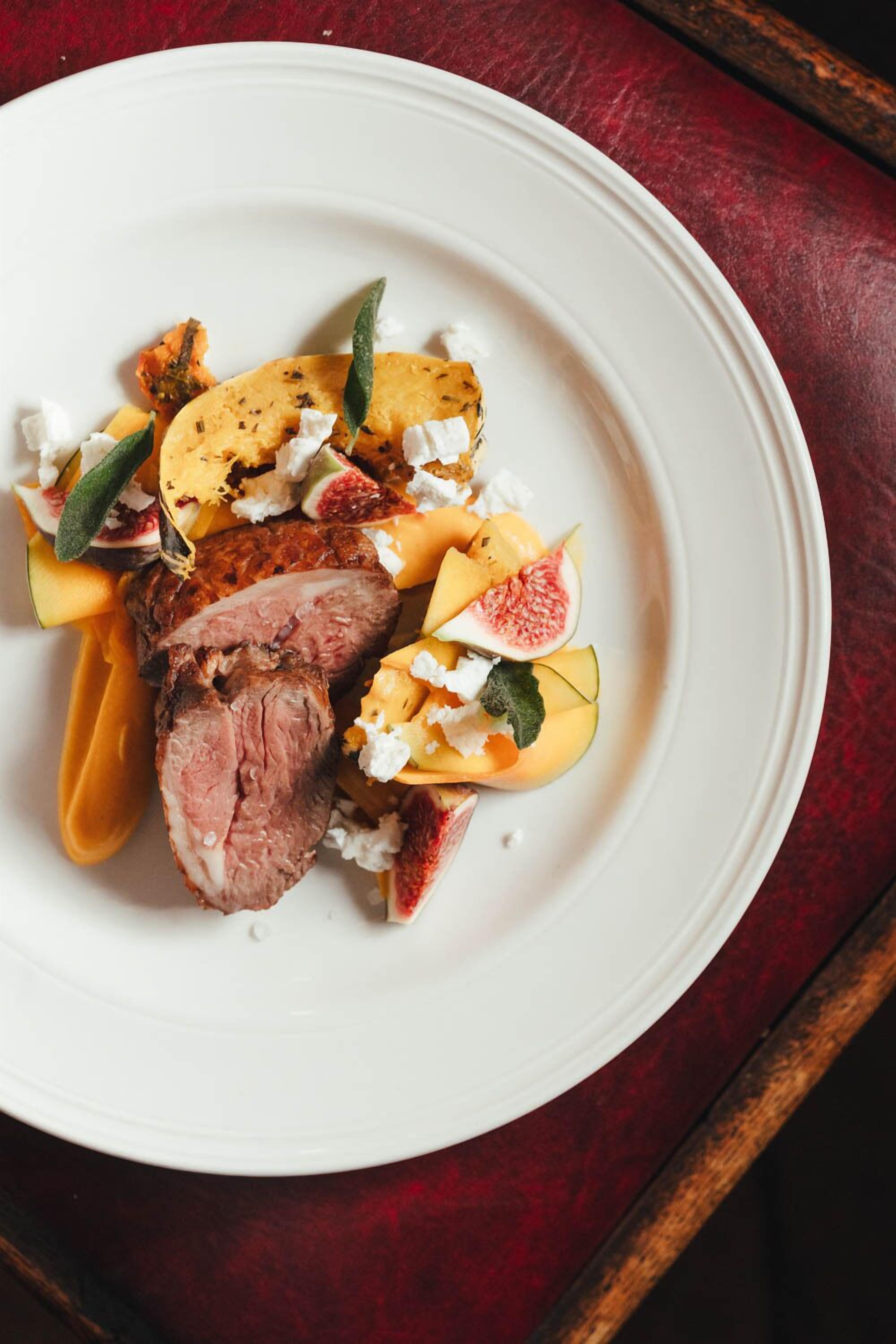 A plate of food with sliced meat, figs, and cheese on a white plate.
