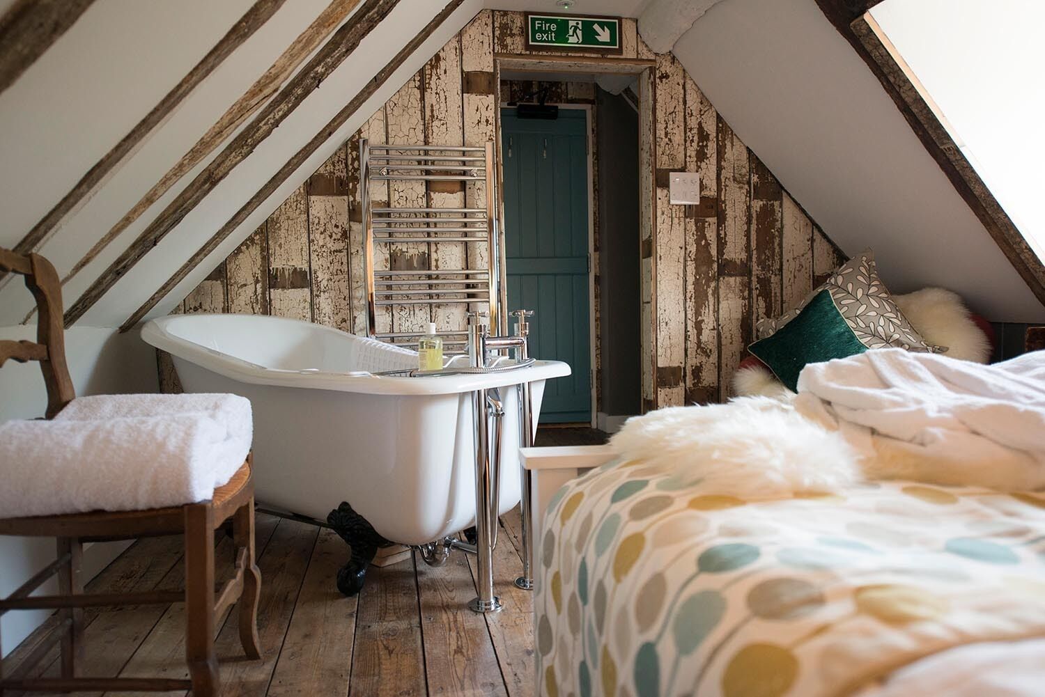 Un dormitorio acogedor en el ático con bañera, piso de madera y cama con edredón de lunares.