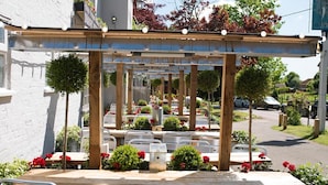 An outdoor seating area with tables and chairs, surrounded by greenery and flowers. - The Woolpack Inn Warehorne (Ashford)