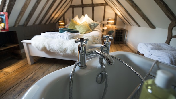 A bedroom with a sloped ceiling, a bed with pillows, a bedside table, and a bathroom with a sink and shower. - The Woolpack Inn Warehorne (Ashford)
