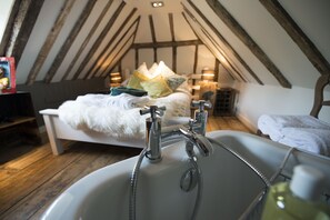 Un dormitorio con techo inclinado, una cama con almohadas, una mesita de noche y un baño con lavamanos y ducha.