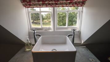 Un baño con un lavabo blanco, una ventana con cortinilla roja y blanca, y vistas al exterior con vegetación.