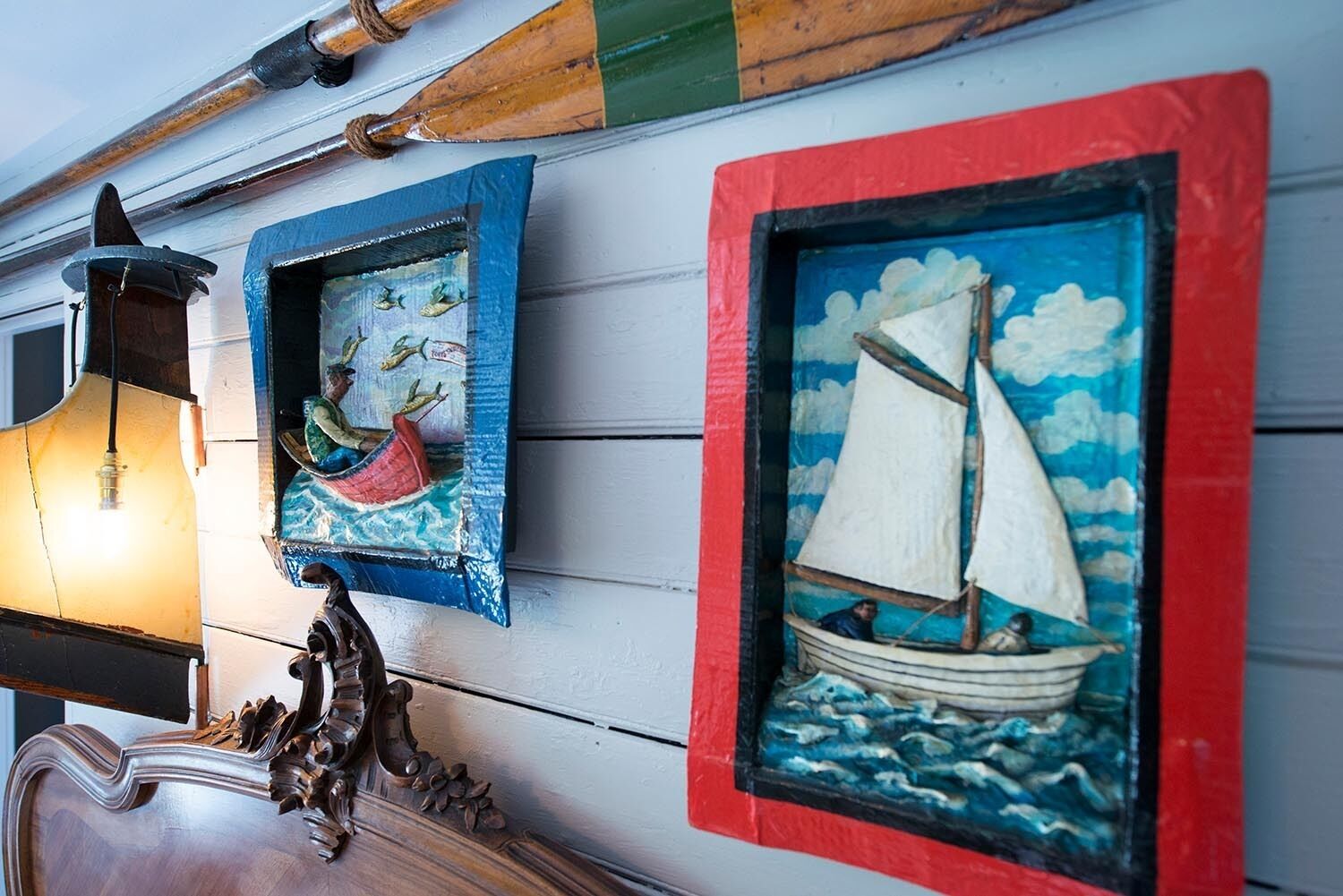 A wall with three framed artworks depicting a canoe, a sailboat, and a lantern.