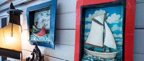A wall with three framed artworks depicting a canoe, a sailboat, and a lantern.