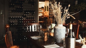 A restaurant interior with a wooden table set for dining, a wine rack in the background, and a decorative vase with dried plants on the table. - The Woolpack Inn Warehorne (Ashford)