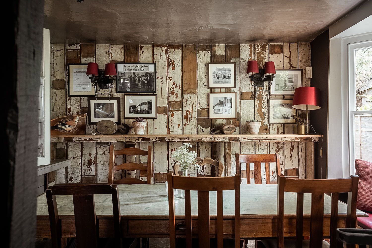A rustic dining area with wooden walls, vintage photographs, and red lamps.