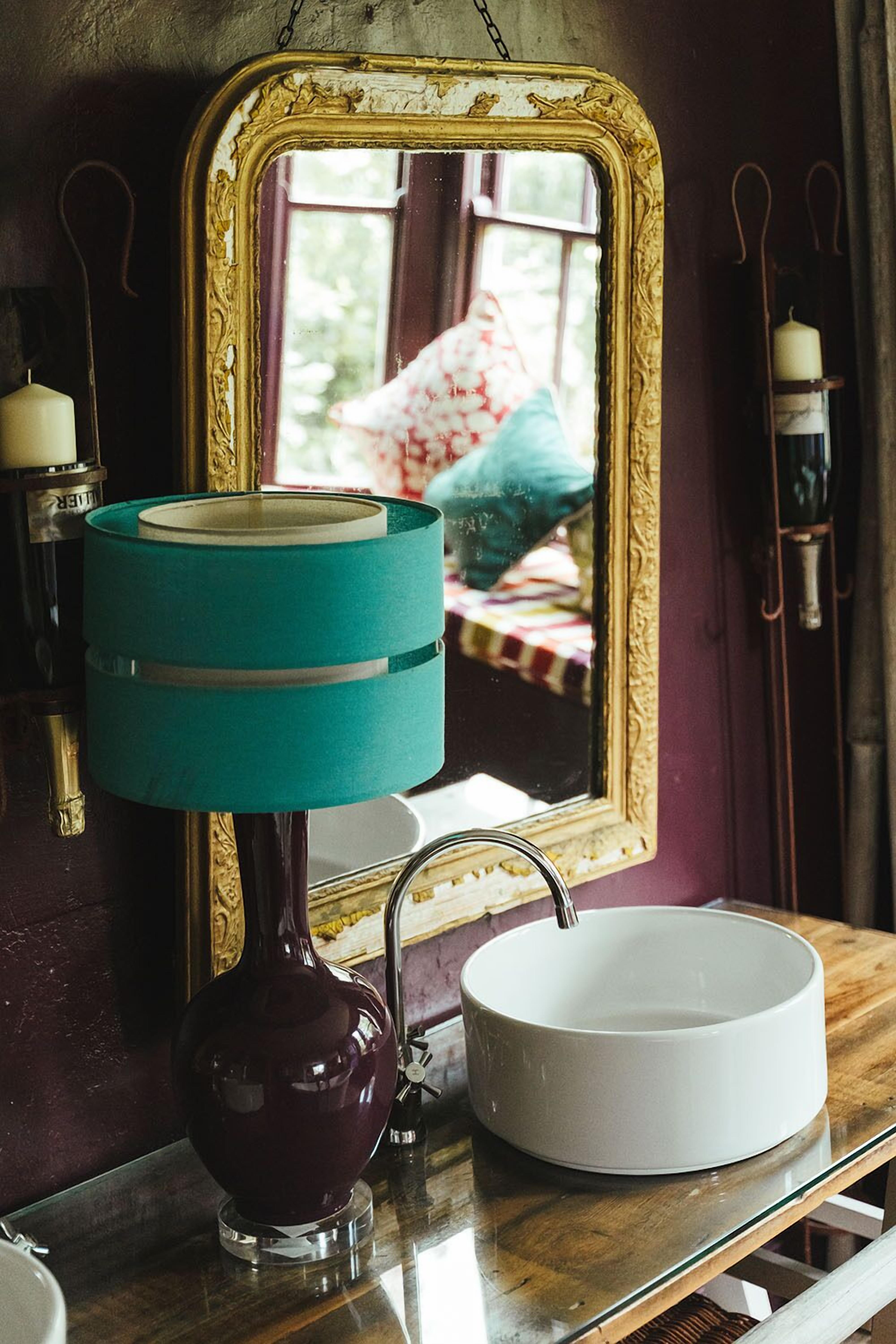 A bathroom with a white sink, a teal-colored lamp, and a gold-framed mirror.