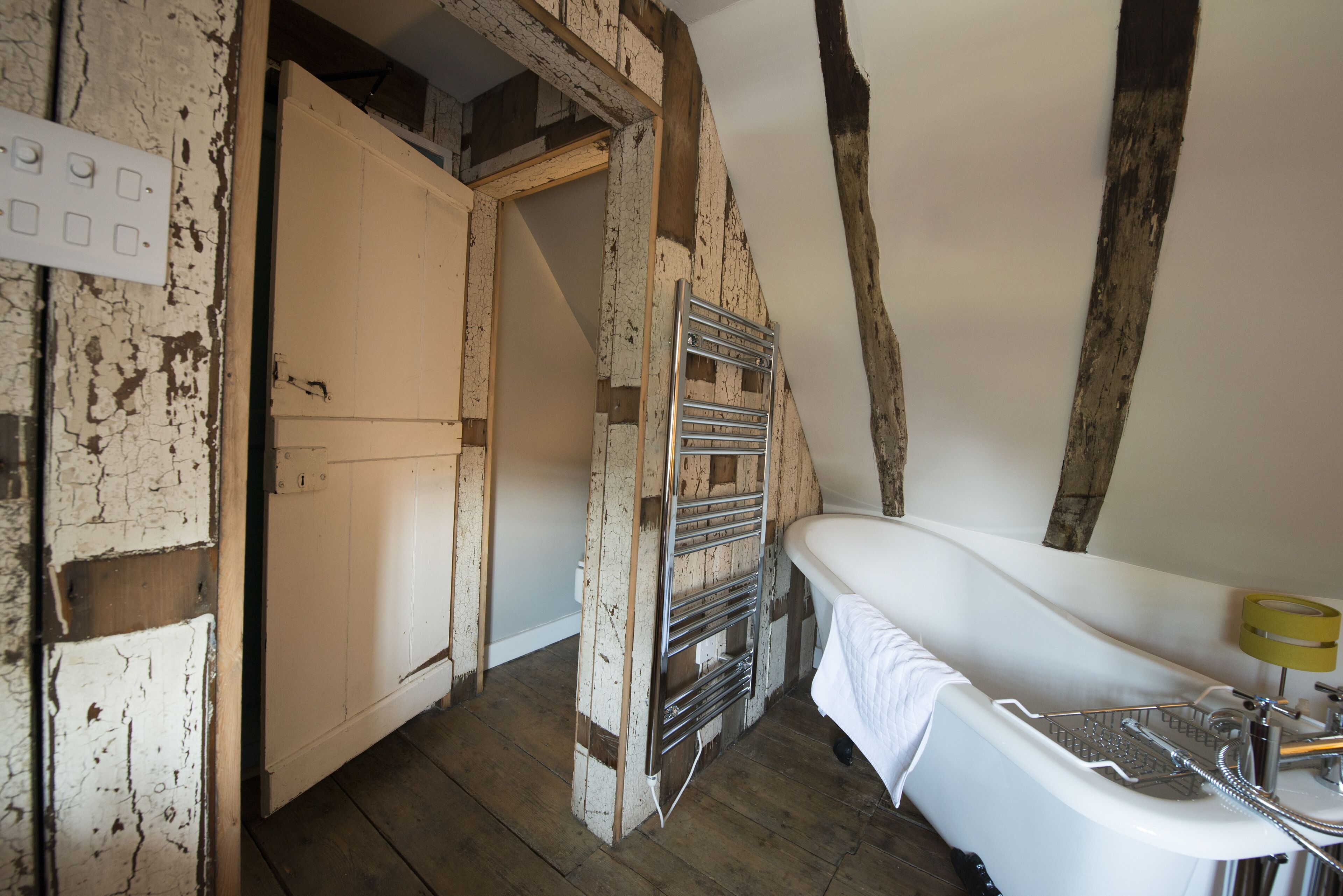 A rustic bathroom with exposed wooden beams, a white bathtub, and a metal towel rack.