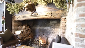 A rustic interior with a brick fireplace, a lion head mounted above it, and a seating area with a table and chairs. - The Woolpack Inn Warehorne (Ashford)