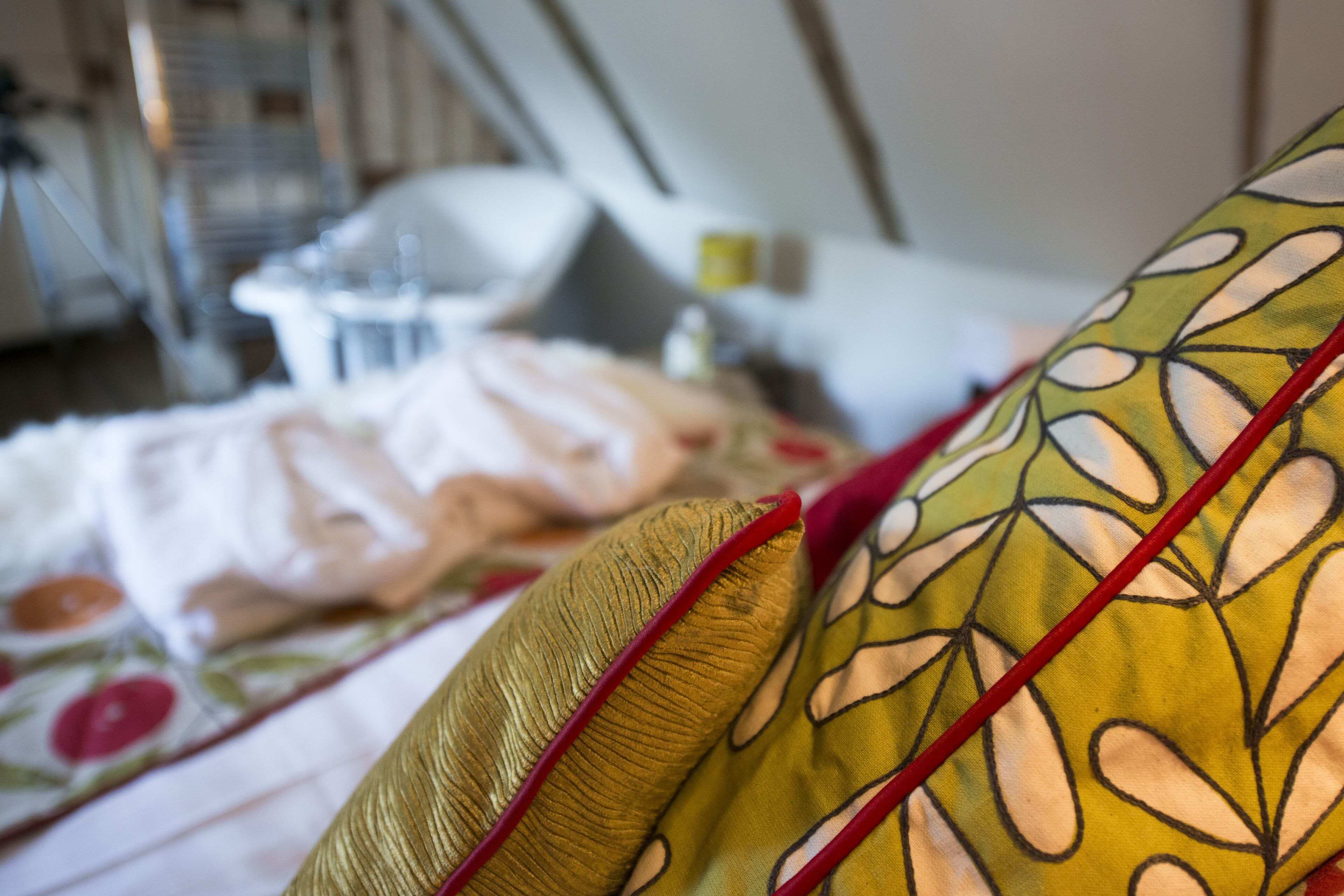 Primer plano de una cama con un cojín estampado de flores y ribete rojo, un cojín blanco y un marco de cama metálico.