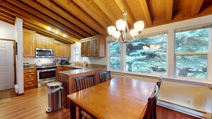 A kitchen with wooden cabinets, a stainless steel microwave, a stove, and a dining area with a wooden table and chairs. - Ranch Condo 3580 -  Elkhorn Resort Amenities (Elkhorn)