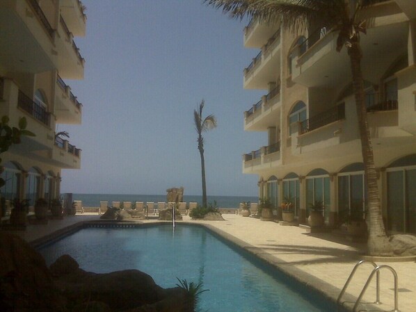 A pool area with lounge chairs, palm trees, and a view of the ocean.