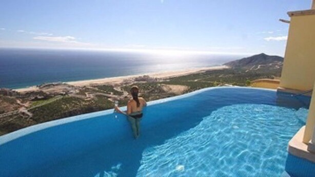 En person i en swimmingpool med udsigt til havet og en strand.
