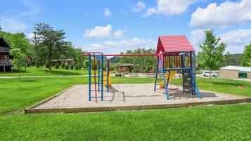 Un'area giochi con strutture per arrampicata e uno scivolo, immersa nel verde dell'erba e degli alberi.