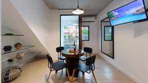 A dining area with a round table, four chairs, a wine bottle, and a television on the wall.