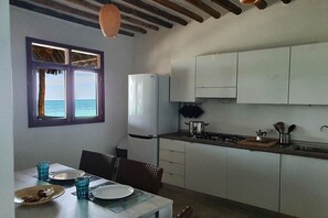 A compact kitchen with white cabinets, a stove, and a window overlooking the sea.