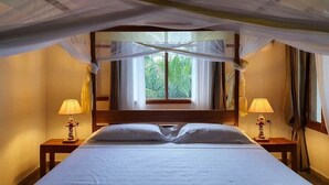A room with a bed, two bedside lamps, a window with curtains, and a canopy.