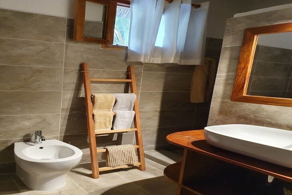 A bathroom with a bidet, a wooden towel rack, a sink, and a mirror.