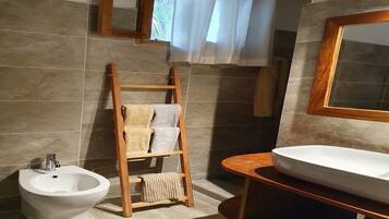 A bathroom with a bidet, a wooden towel rack, a sink, and a mirror.