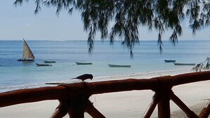 A beach with a wooden fence, a sailboat, and several small boats in the water.