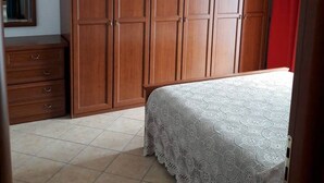 Un dormitorio con un armario grande, una cama con colcha estampada y una cortina roja.