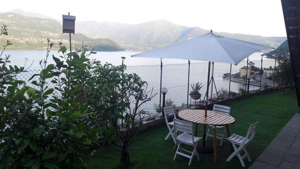 Un patio con mesa y sillas, un paraguas grande y vistas a un lago y montañas.