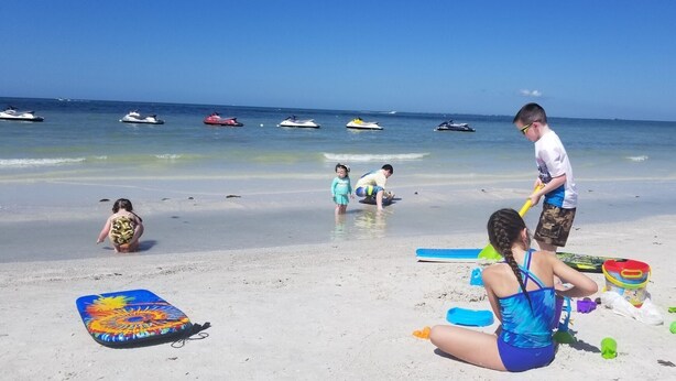 A beach scene with people playing and a jet ski in the background.