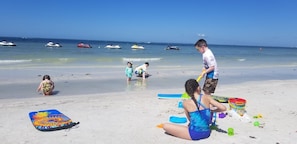 A beach scene with people playing and a jet ski in the background. - Santa Maria awaits you! Large heated pool! (Fort Myers Beach)