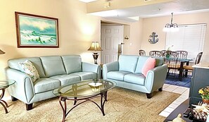 A living room with two sofas, a glass coffee table, a dining table with chairs, and a painting on the wall. - Santa Maria awaits you! Large heated pool! (Fort Myers Beach)