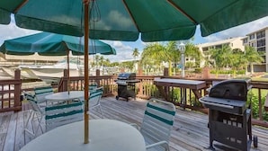 An outdoor patio with green umbrellas, white and green striped chairs, and a barbecue grill.
