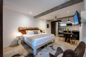 A modern bedroom with a wooden headboard, a white bed, a round bedside table with a lamp, and a cowhide rug. - Zona Romantica Beautiful Modern Studio (Emiliano Zapata)