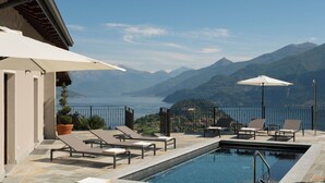 A poolside area with lounge chairs and umbrellas, overlooking a lake and mountains.