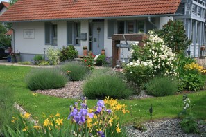 A house with a garden in front, a red-tiled roof, and a sign on the door. - Multi-bed room 1 with WC and shower, air-conditioned - Gästehaus Hauser (Rust)