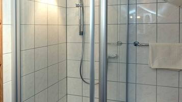 Et moderne badeværelse med en brusekabine i glas, hvide flisevægge og en lille, hvid skammel.