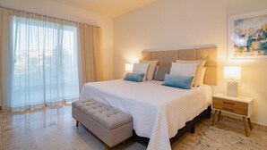 A bedroom with a large bed, bedside lamps, a bench, and a painting on the wall. - Paraiso Del Mar Resort E202 2 Bed by Casago (La Paz)