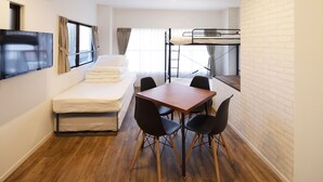 Une chambre compacte comprenant un lit superposé, un téléviseur à écran plat, une petite table à manger avec des chaises et un canapé.