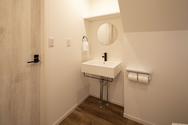 A bathroom with a white sink, a round mirror, a towel hanging on a hook, and a toilet paper holder.