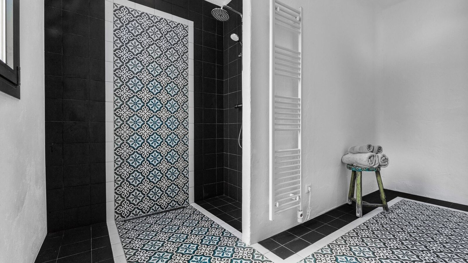 Une salle de bain avec des carreaux noirs et blancs formant un motif, un porte-serviettes blanc et un petit tabouret sur lequel sont posées des serviettes.