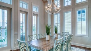 Une salle à manger avec une table en bois, six chaises, deux plantes en pot et un lustre.