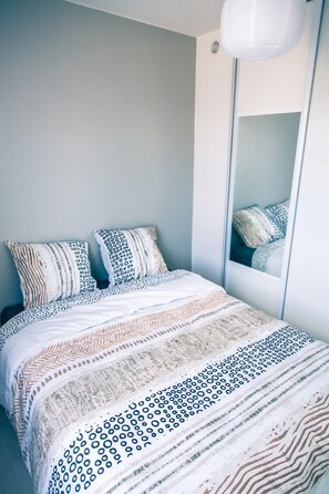 Ein Schlafzimmer mit einem Bett, zwei Kissen mit Muster, einem großen Spiegel und einer Pendelleuchte.