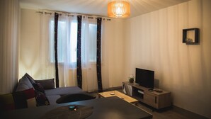 Una sala de estar moderna con un sofá, una mesa de centro, un televisor sobre un mueble de madera y una lámpara colgante.