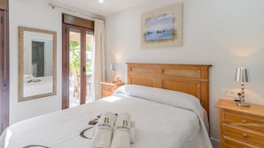 Un lit bien fait, avec un cadre à carreaux, un tableau accroché au-dessus, et une table de chevet en bois sur laquelle se trouve une lampe.