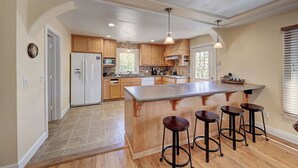 A spacious kitchen with wooden cabinets, a central island with stools, and a refrigerator. - 1927 - Murphys Vacation Rentals (Murphys)