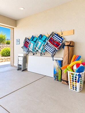 A poolside area with multiple pool chairs, a trash bin, and a basket containing pool toys.