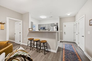 Een moderne keuken met een magnetron, oven en barstoelen. Drie deuren leiden naar andere ruimtes.