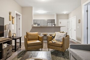Een woonkamer met twee leren fauteuils, een salontafel, een televisie en een keukenhoek met kasten en apparatuur.