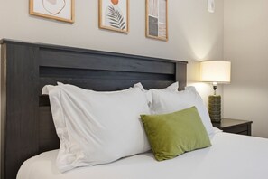 Une chambre d’hôtel comprenant un lit, des oreillers, une table de chevet, une lampe et des œuvres d’art mural.