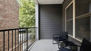 Un balcon avec une balustrade en métal, deux chaises et une fenêtre avec des stores.
