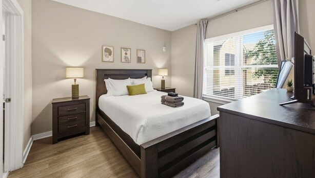 Une chambre d’hôtel équipée d’un lit, de lampes de chevet, d’un bureau avec un ordinateur et d’une fenêtre avec des stores.