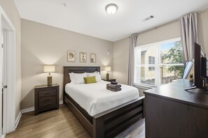 Hotelkamer met een bed, nachtlampjes, een bureau met een computer en een raam met zonwering.
